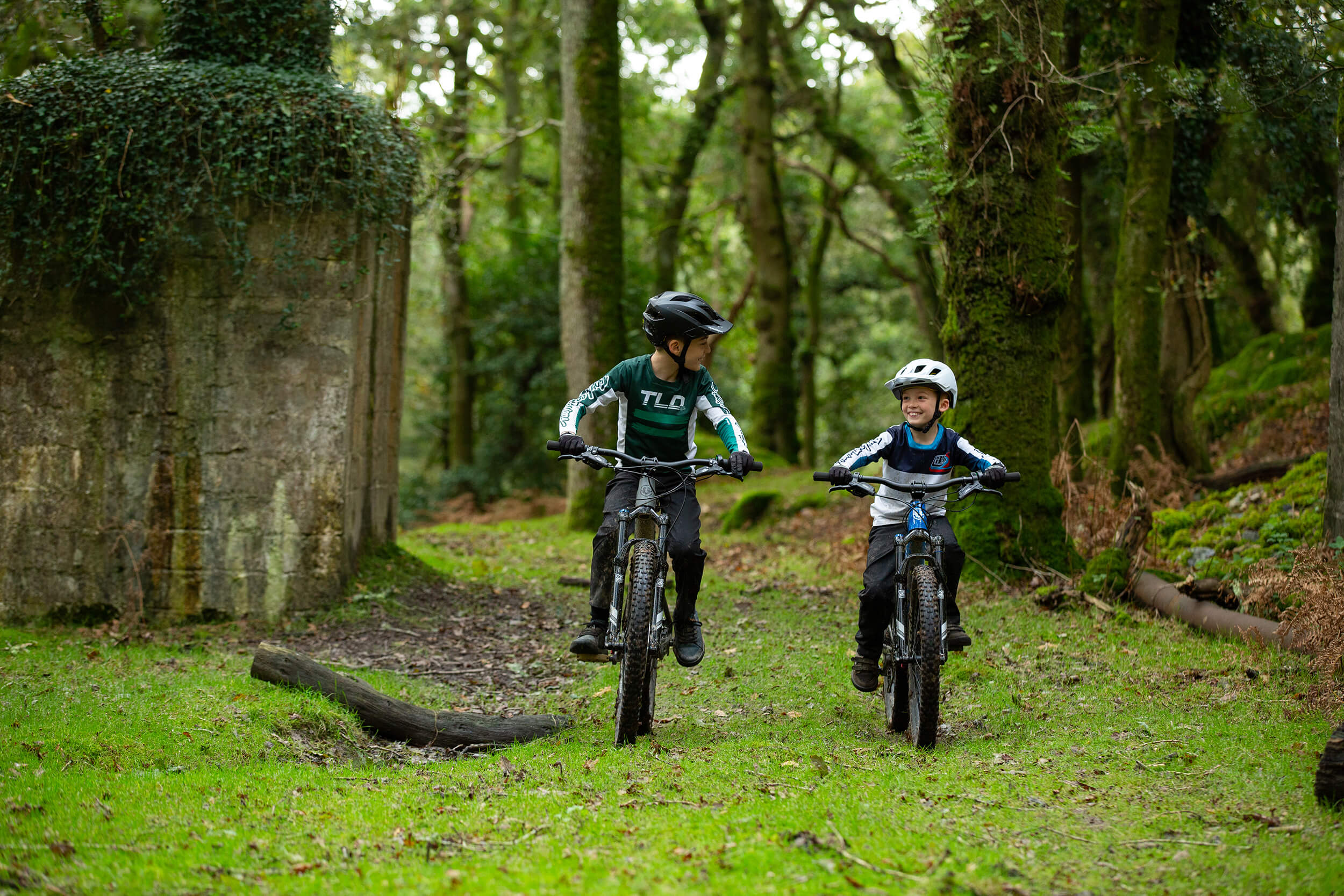 Kinder fahren Mondraker-Kids-Mountainbikes im Wald, mit Helmen und sportlicher Kleidung, geeignet für junge Radsportler.