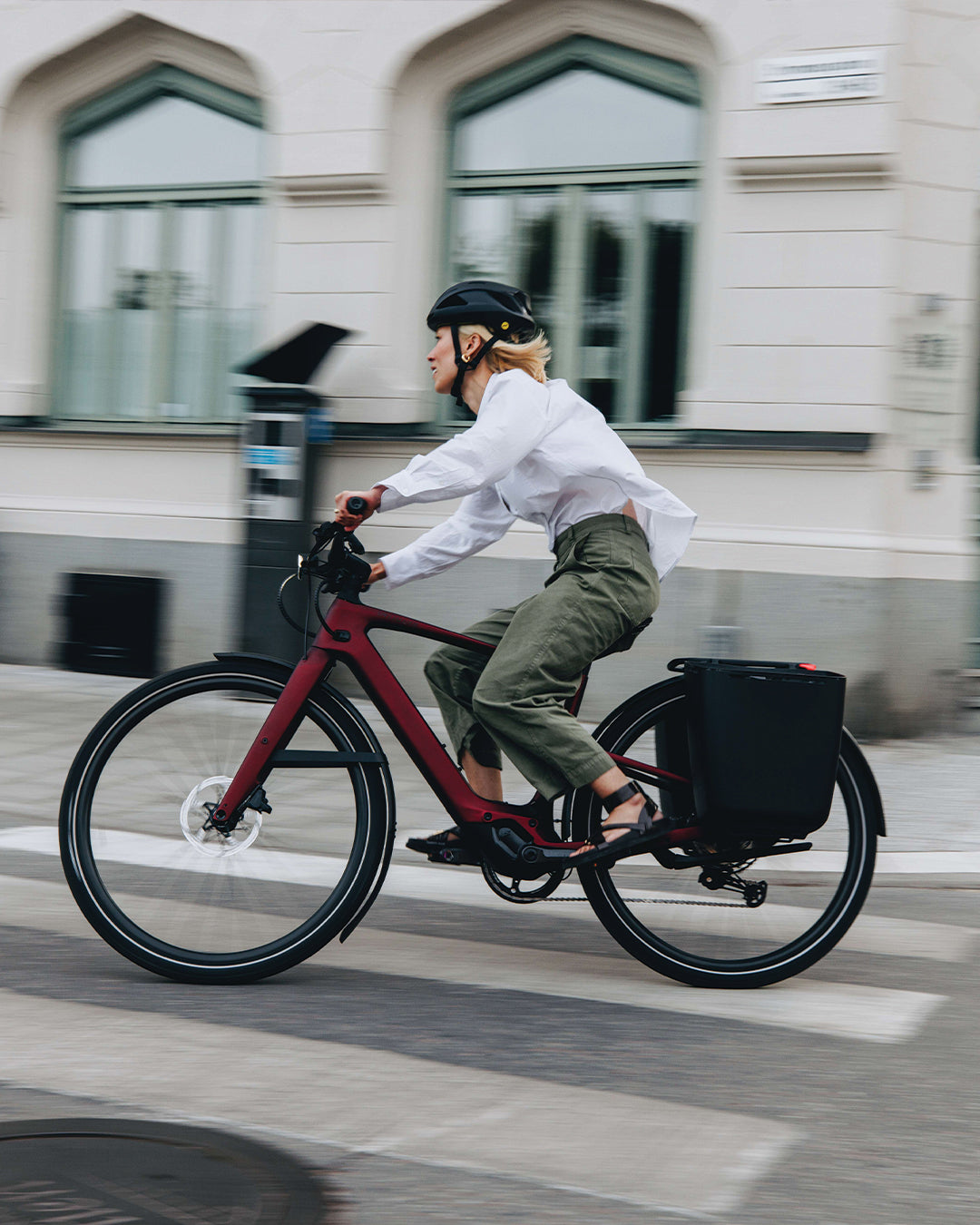 Frau fährt Specialized Turbo Vado E-Bike in der Stadt, trägt Helm und hat Gepäcktasche auf dem Rad. Ideal für Pendler.