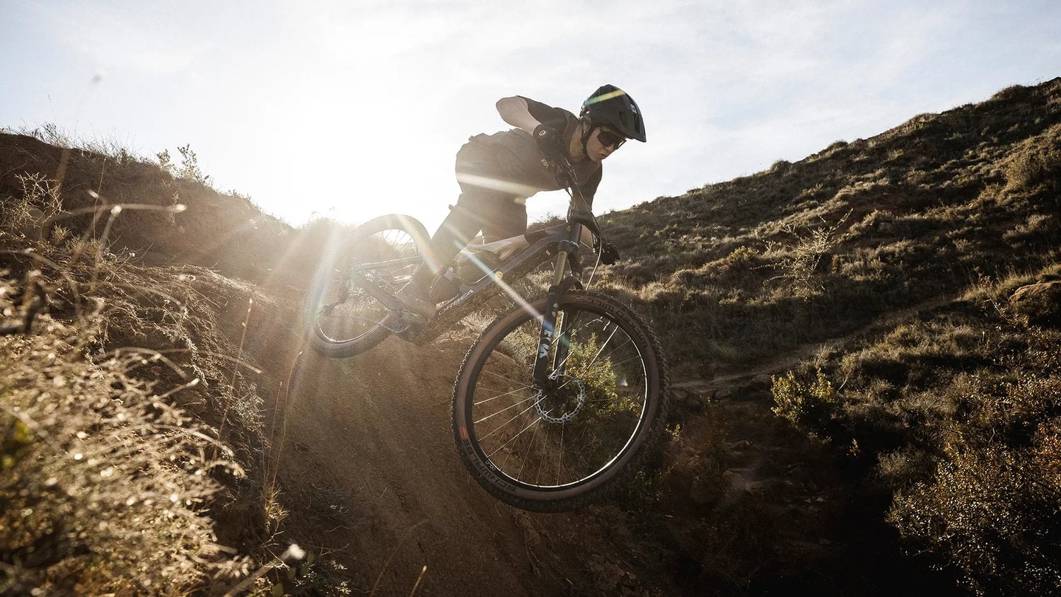 Ein Mountainbiker fährt steil bergab auf einem Orbea Rise E-Bike in einer sonnendurchfluteten Landschaft.