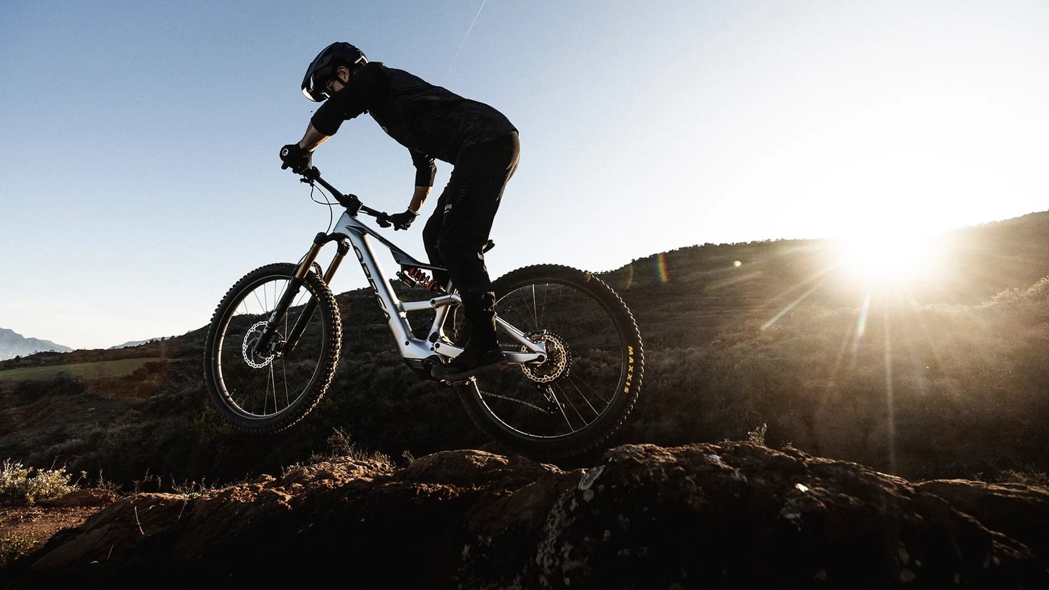 Person auf einem Orbea Rise E-Mountainbike fährt über felsiges Gelände bei Sonnenuntergang.