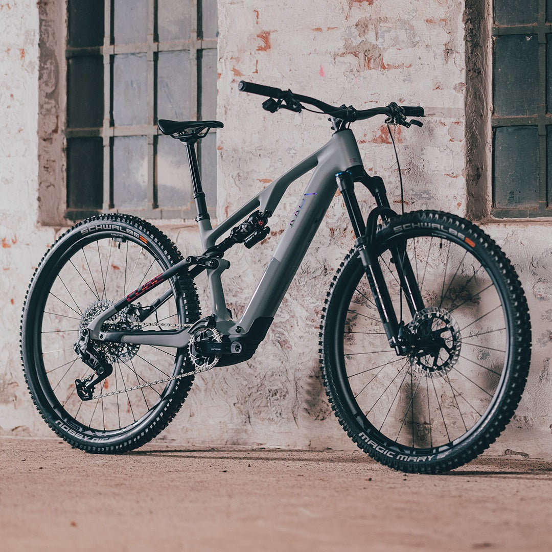 Graues Mountainbike Cube AMS Hybrid ONE44 vor Backsteinwand, geeignet für Offroad-Abenteuer.