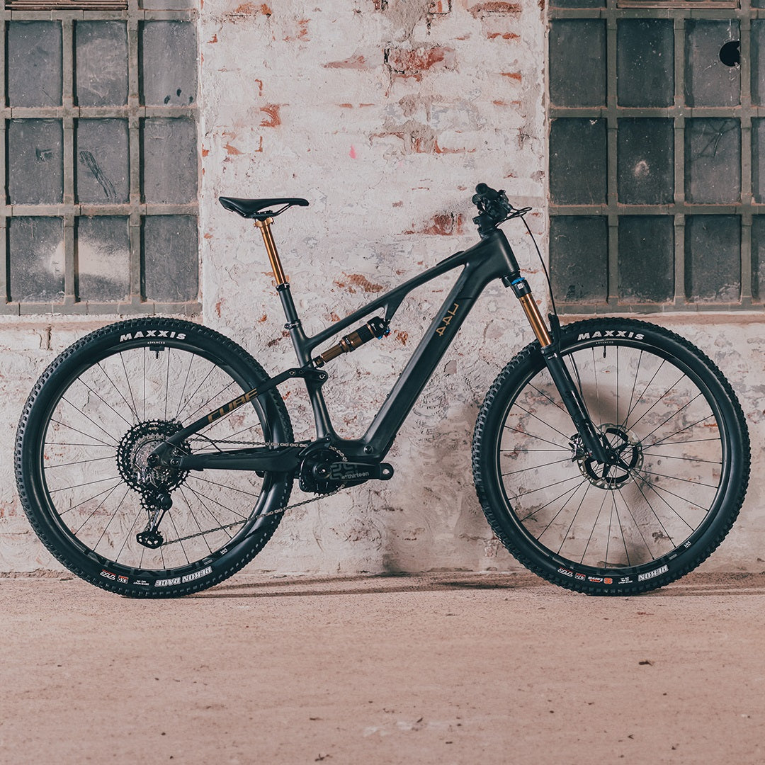 Schwarzes Cube AMS Hybrid One44 E-Mountainbike vor rustikaler Backsteinwand.