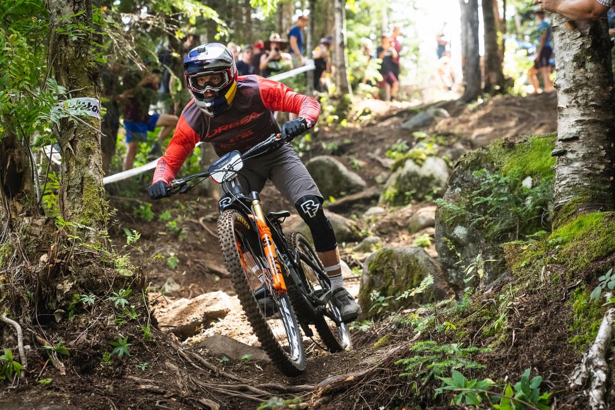Mountainbiker mit Orbea Rallon radelt schnell durch einen bewaldeten Trail, umgeben von Zuschauern.