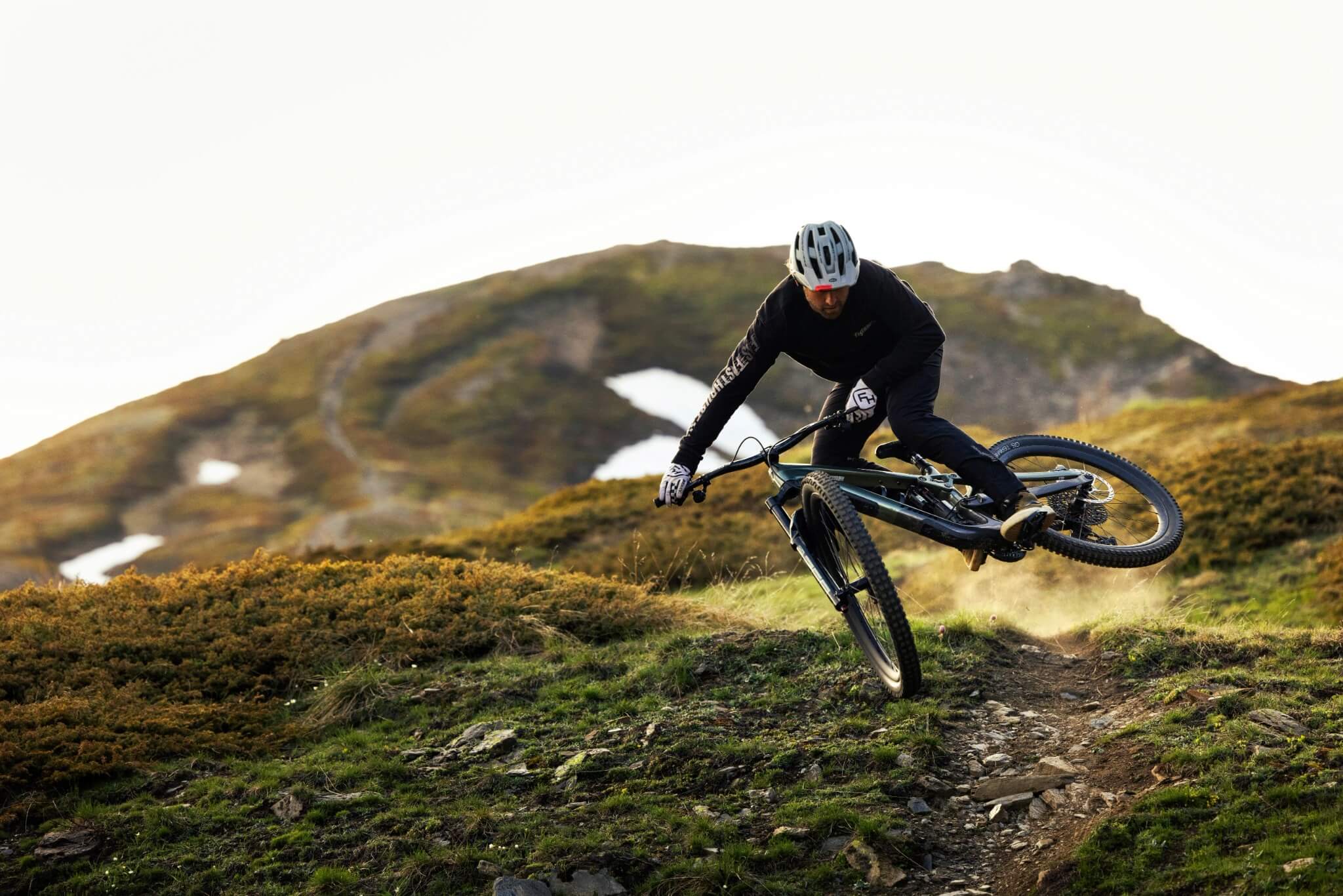 Mountainbiker auf Trek Fully, steinigem Weg, hügelige Landschaft, Vorderrad trickreich in der Luft, dynamische Pose.