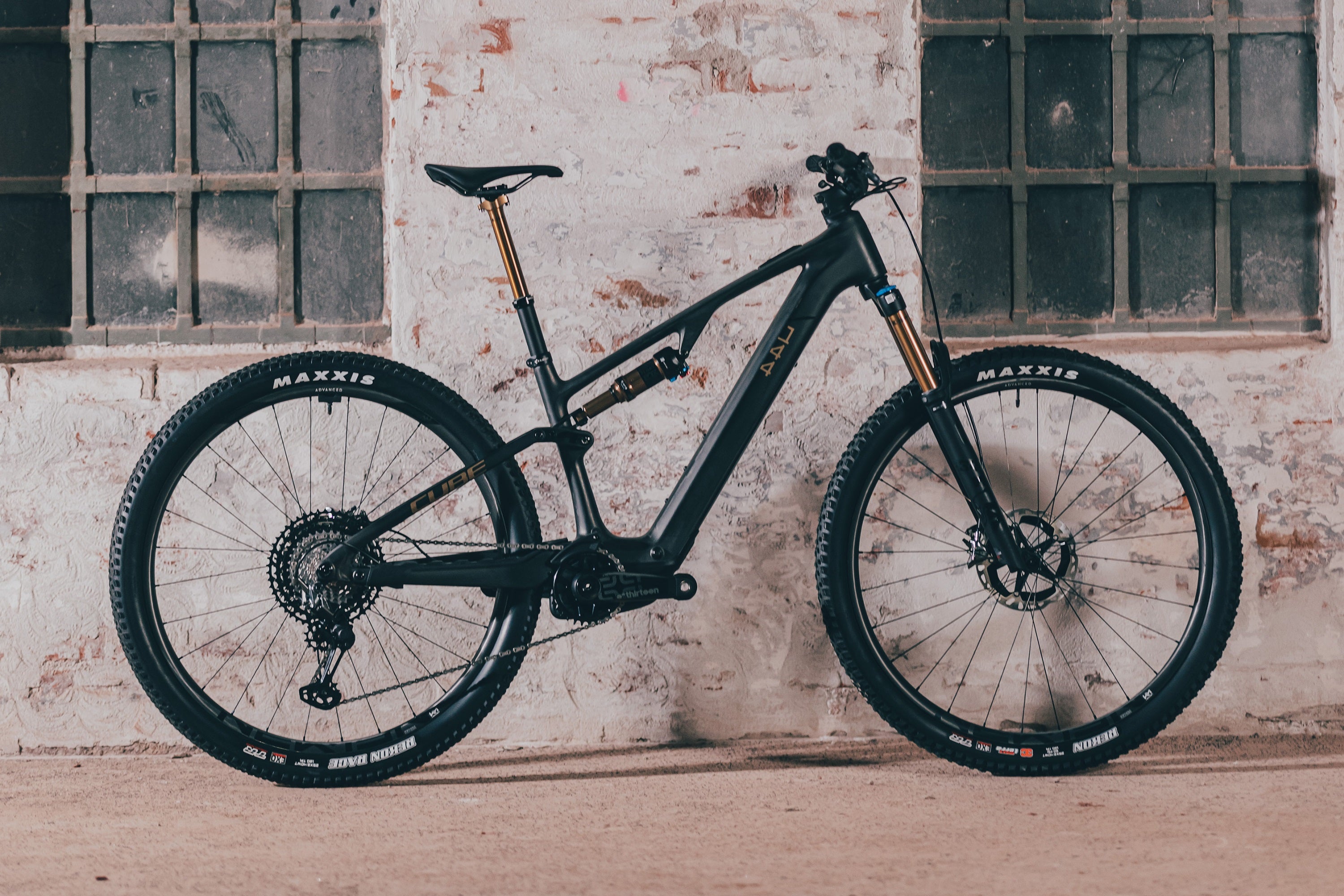 Schwarzes Cube E-Mountainbike Fully vor Backsteinmauer, geeignet für Offroad- und Geländeabenteuer, Maxxis-Reifen.