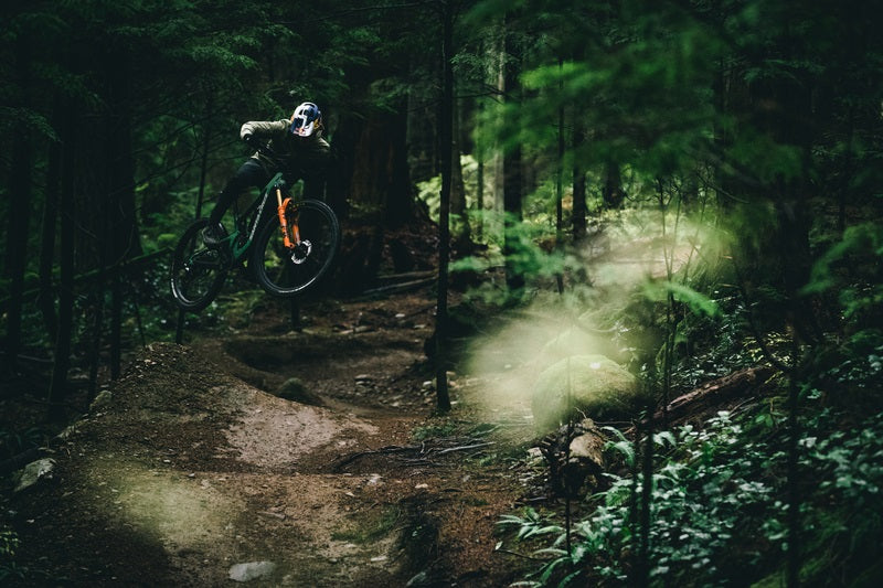 Rider auf Santa Cruz Mountainbike springt im dichten Wald auf einem schmalen Pfad.
