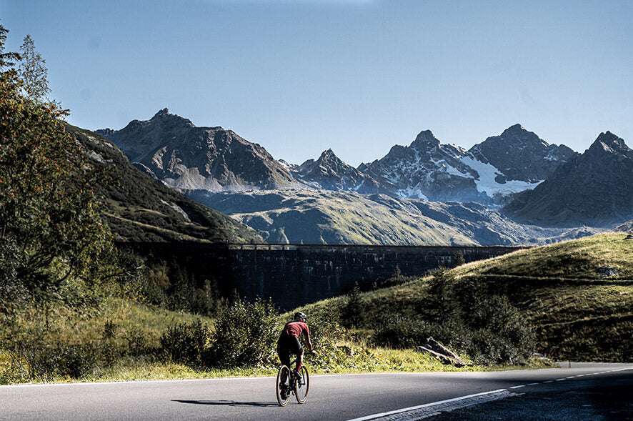 Radfahrer fährt auf Specialized Rennrad in alpiner Landschaft bei sonnigem Wetter.