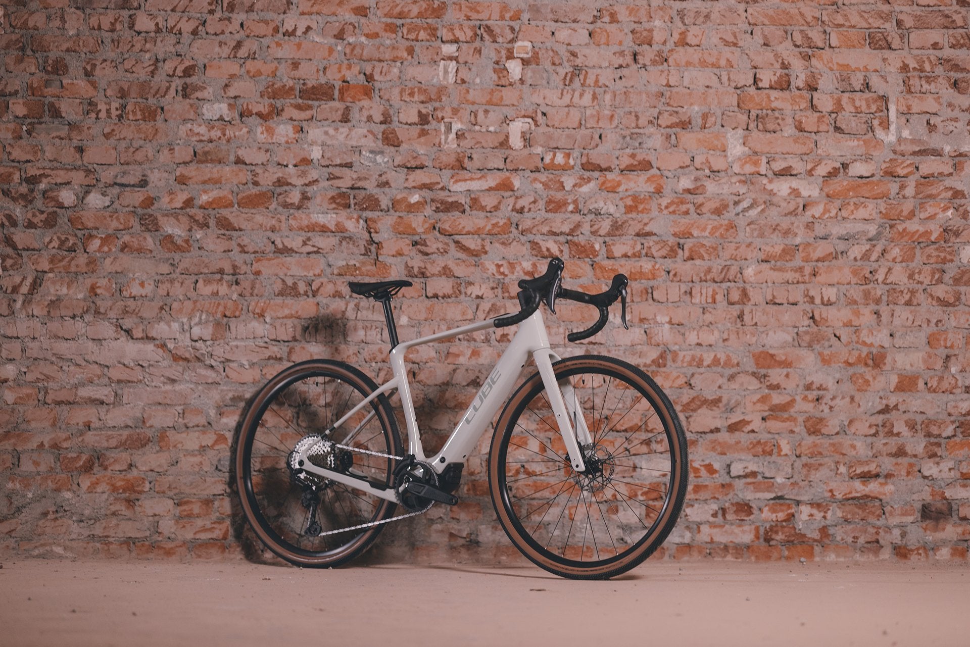 Cube Nuroad Hybrid E-Bike an alter Ziegelwand, geeignet für Straßen- und Geländefahrten, sportliches Design.