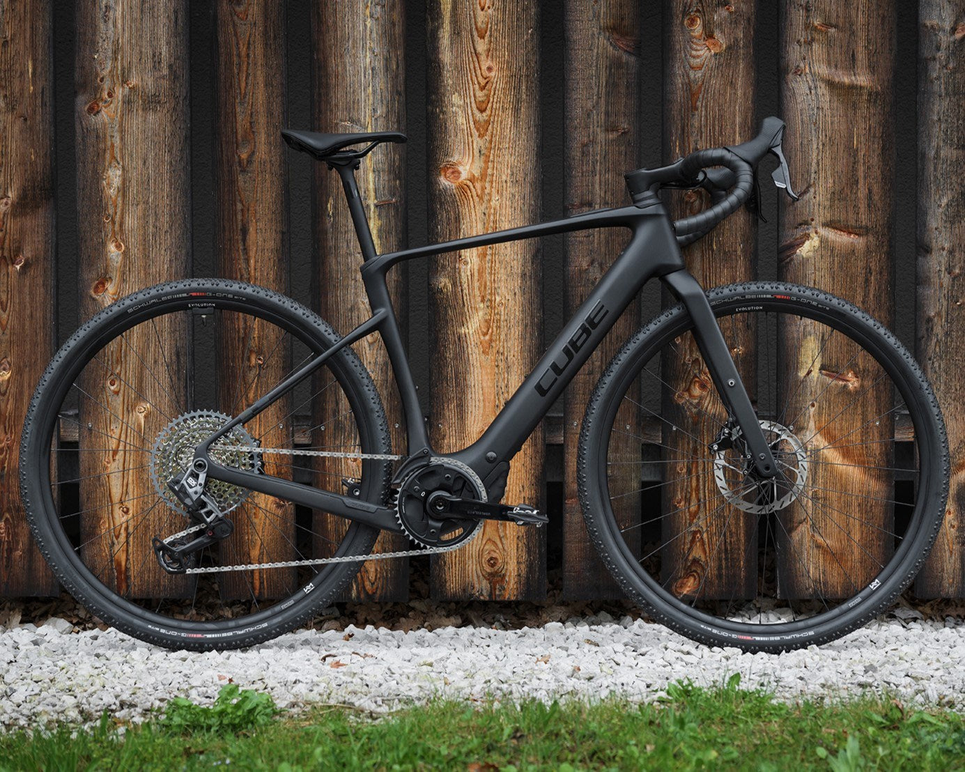 Schwarzes Cube Nuroad Hybrid Gravelbike vor Holzwand, geeignet für Abenteuer und sportliche Fahrten auf verschiedenen Untergründen.
