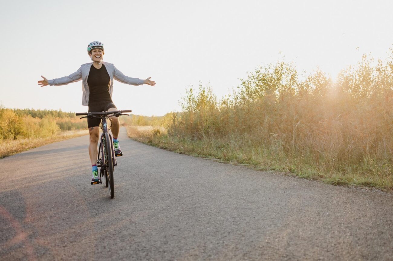 Person fährt glücklich auf einem Fahrrad auf einer Landstraße, Arme ausgebreitet; Specialized City und Urban.