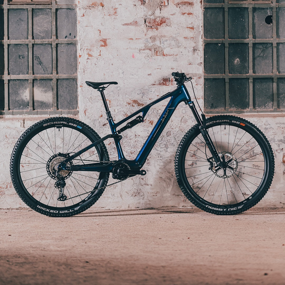 Blaues Cube AMS Hybrid ONE44 E-Mountainbike, stehend vor einer Ziegelwand, ideal für Offroad-Abenteuer.