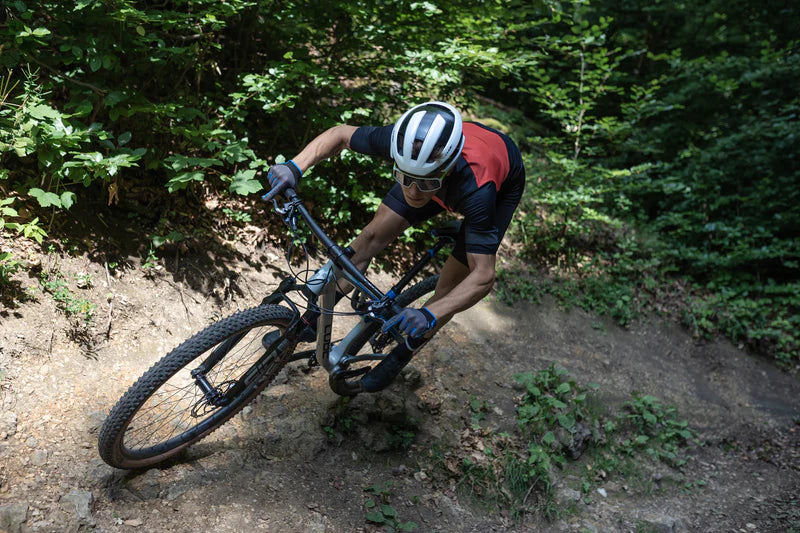 Mountainbiker fährt mit einem Cube Fully auf einem Waldtrail bergab, passende Ausrüstung für Outdoor-Enthusiasten.