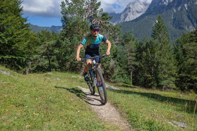 Radfahrer*in auf Cube Hardtail Mountainbike, fährt auf einem Waldpfad in Berglandschaft. Ideal für Offroad-Abenteuer.