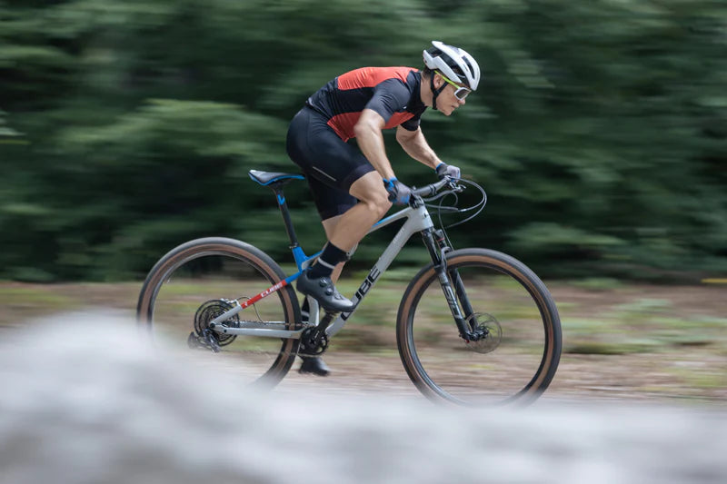 Rennradfahrer auf CUBE Mountainbike im Wald, trägt Helm und Sportbekleidung, konzentriert auf Geschwindigkeit und Kontrolle.