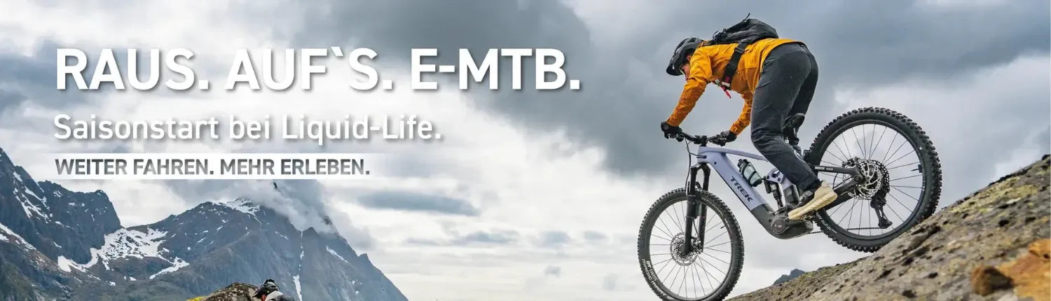 Person auf Trek E-Mountainbike fährt einen steinigen Bergpfad hinauf; Wolken und Berge im Hintergrund. Text: „RAUS. AUF‘S. E-MTB.“