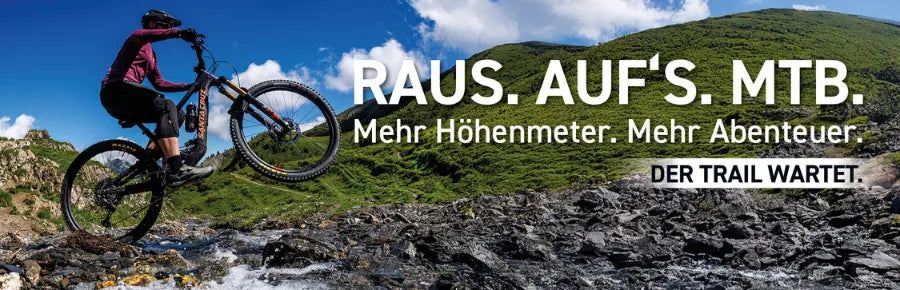 Mountainbiker überquert steinigen Fluss vor grüner Landschaft. Text: "Raus. Auf's. MTB. Der Trail wartet."