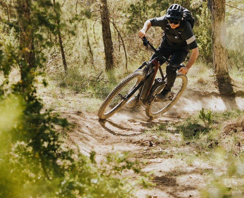 Mountainbiker auf einem Trail im Wald, trägt Helm und Brille, auf einem schwarzen E-Mountainbike von page.light-e-bikes.