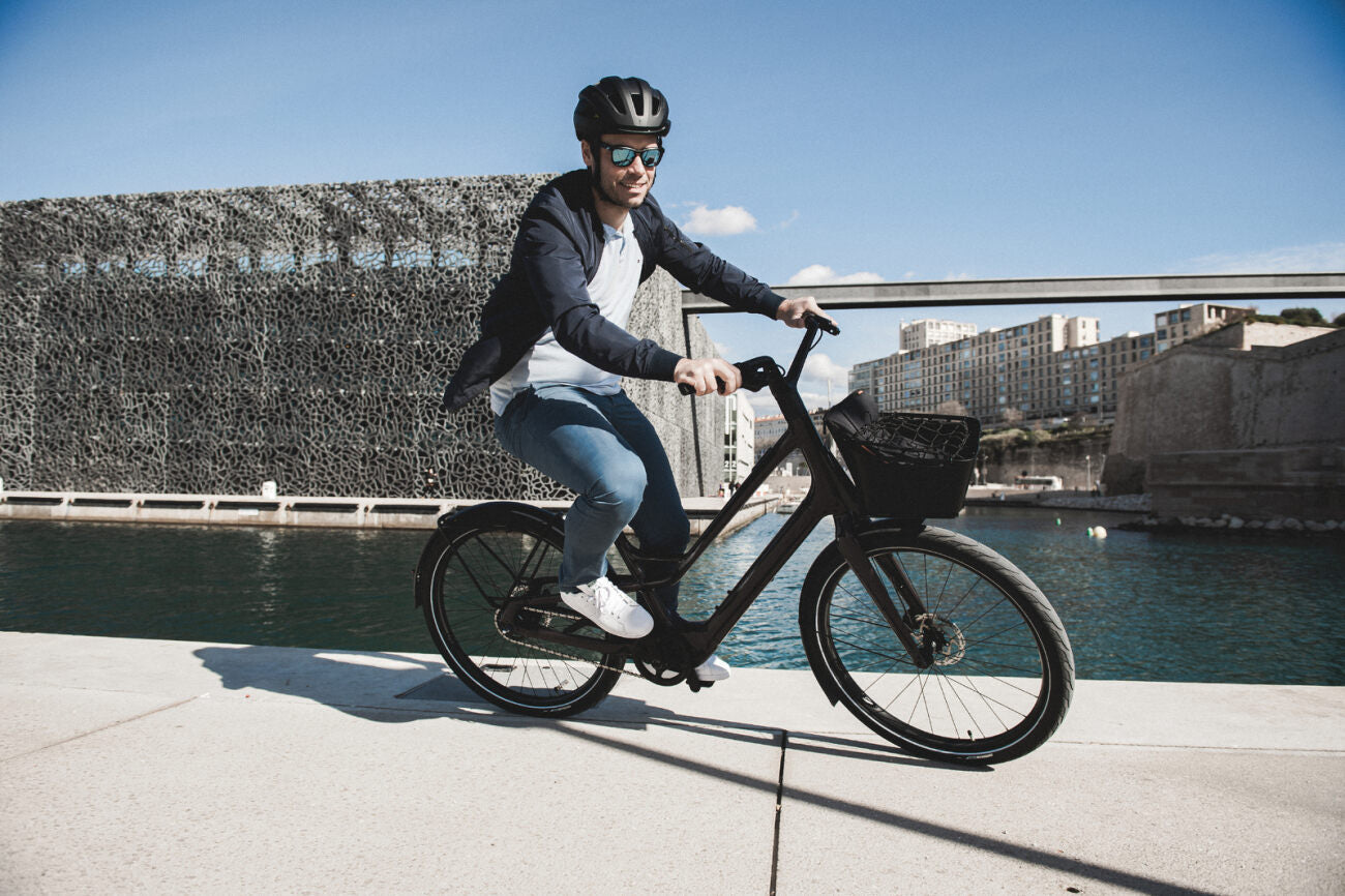 Mann auf einem E-City-Urban-Fahrrad fährt in städtischer Umgebung entlang des Wassers.