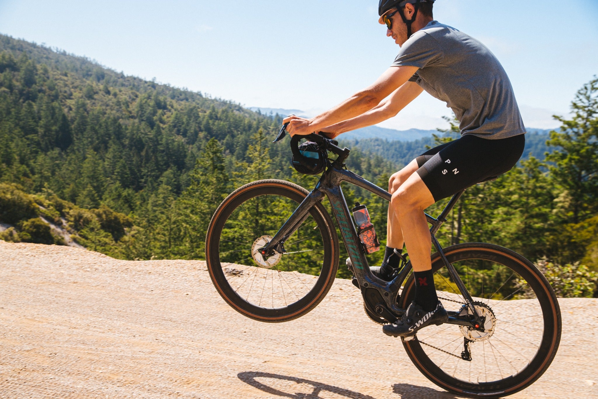 Mann auf einem Light-E-Bike fährt eine Schotterpiste entlang, umgeben von Wald und Bergen.