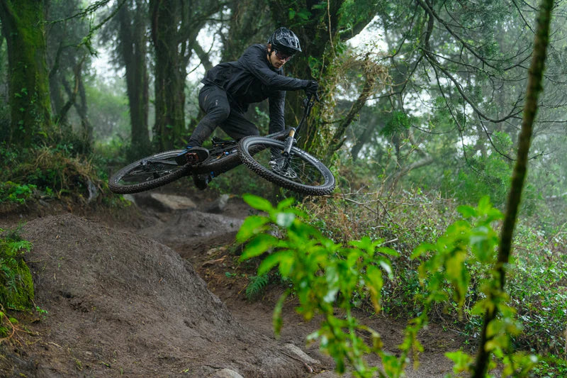 Mountainbiker springt mit Cube Fully in Wald, trägt Schutzkleidung. Offroad-Einsatz für anspruchsvolle Trails geeignet.