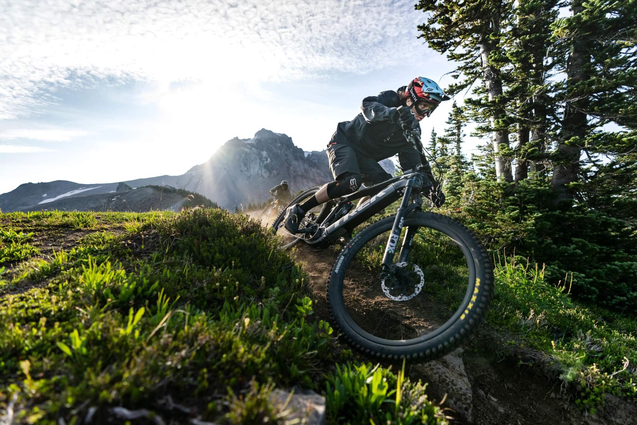 Mountainbiker fährt ein Trek Rail E-Bike auf einem Waldweg bergab, begleitet von atemberaubender Berglandschaft.