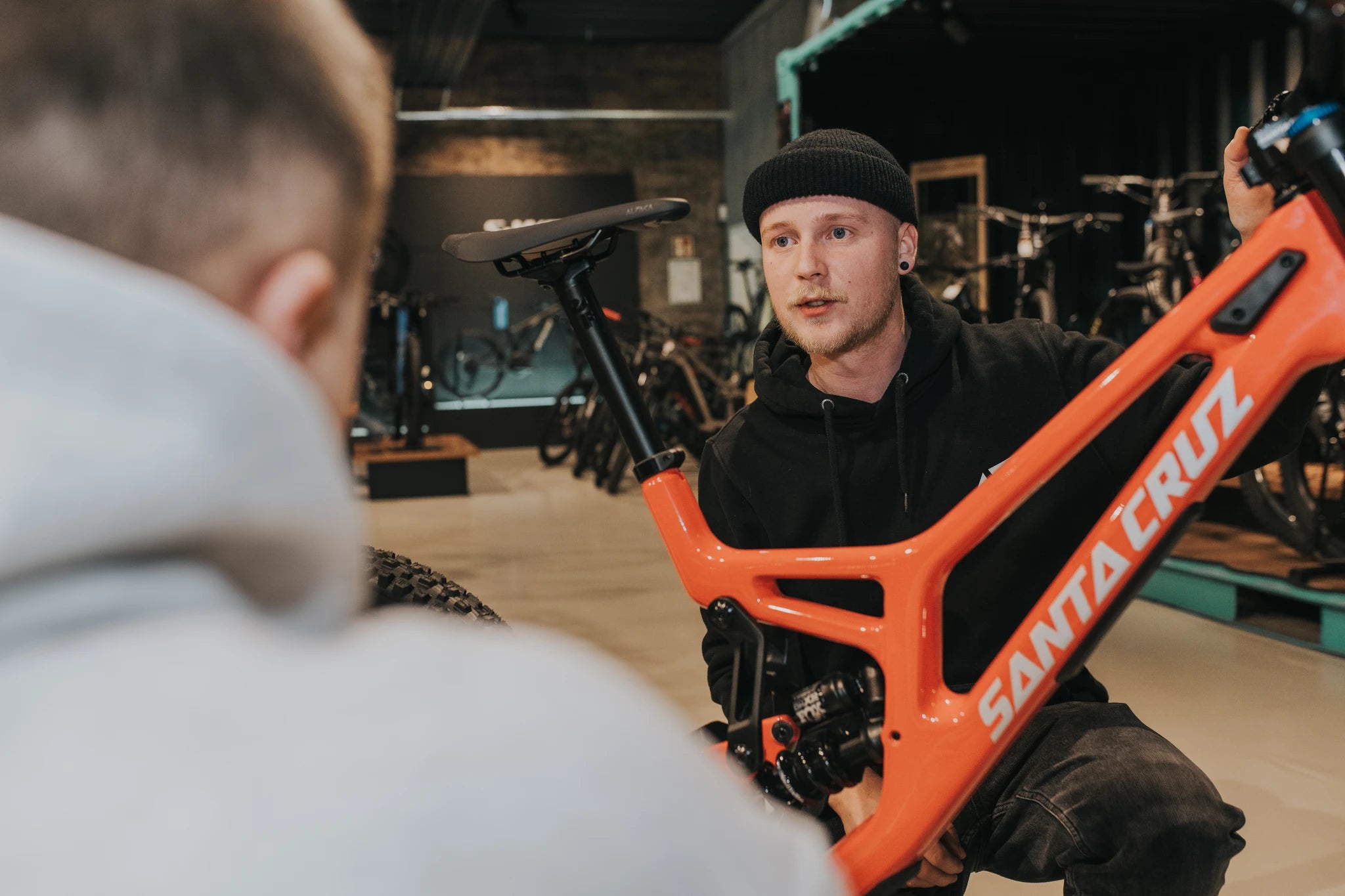 Verkäufer zeigt rotes Santa Cruz Mountainbike in Fahrradgeschäft, Beratung im Vordergrund. Zielgruppe: Mountainbiker.