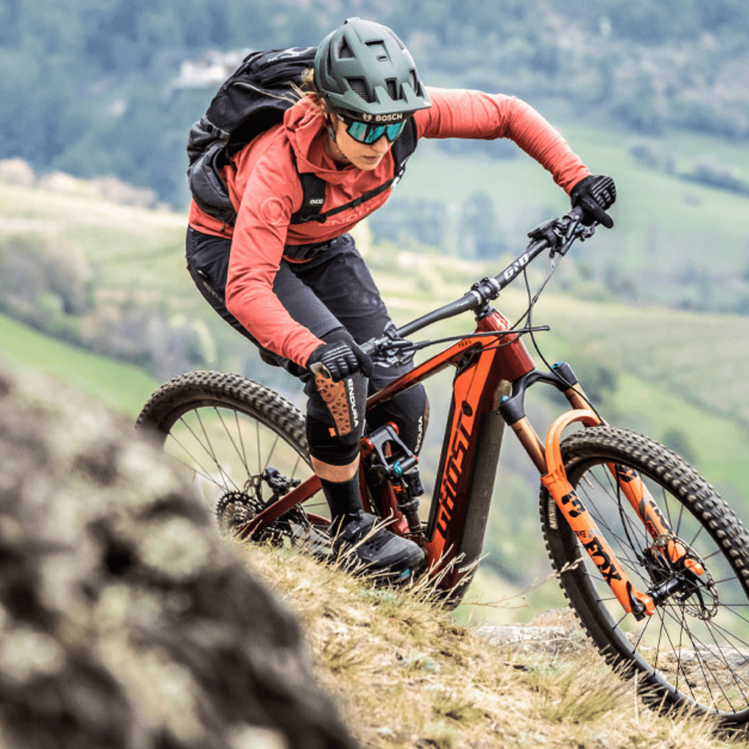 Person auf einem Moustache-E-Mountainbike, Modell Samedi, in roter Kleidung, fährt einen steilen Hang hinunter.