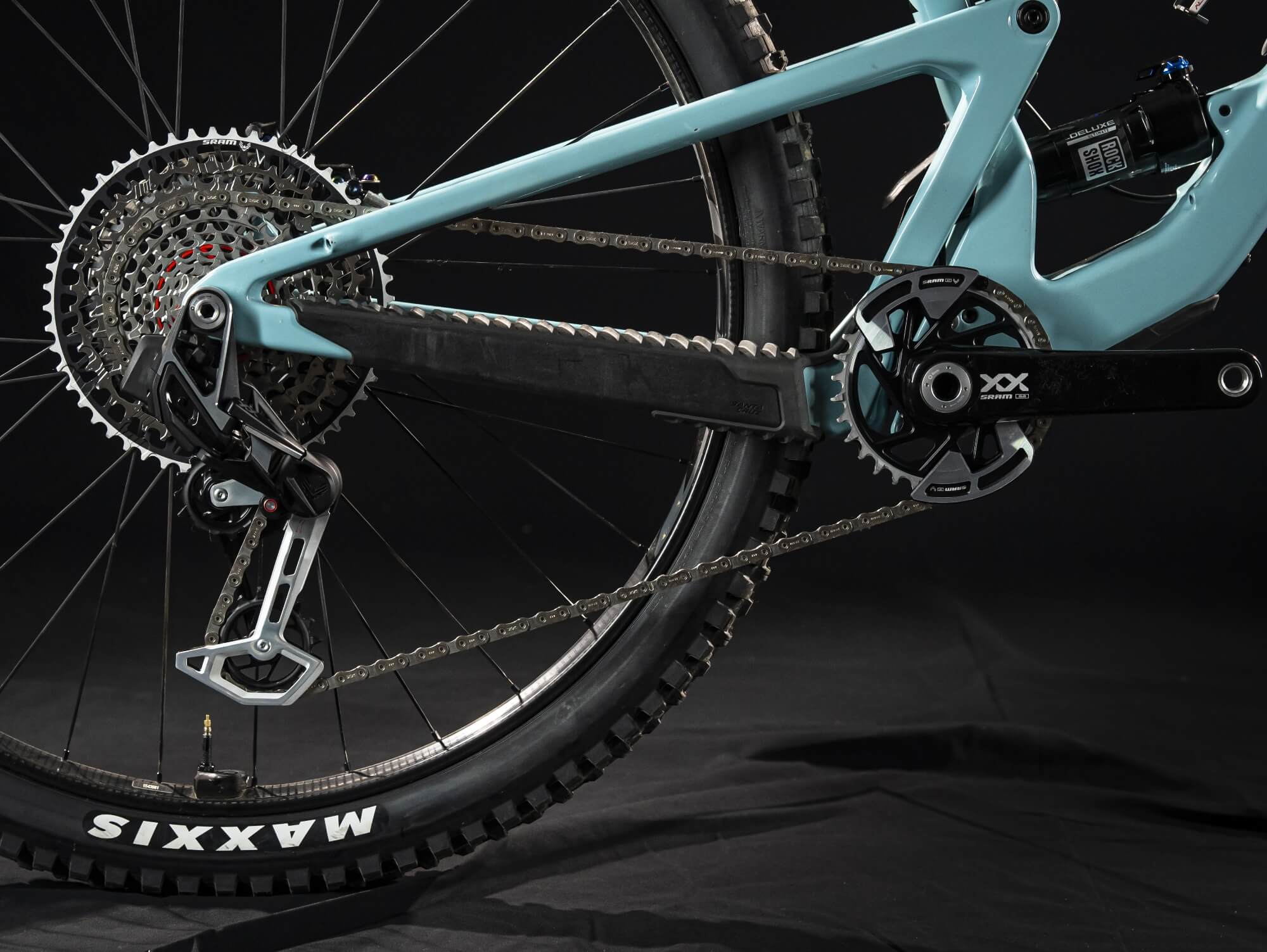 Nahaufnahme eines SRAM MTB-Antriebs mit Kassette, Kurbelgarnitur und Kette auf einem hellblauen Rahmen.