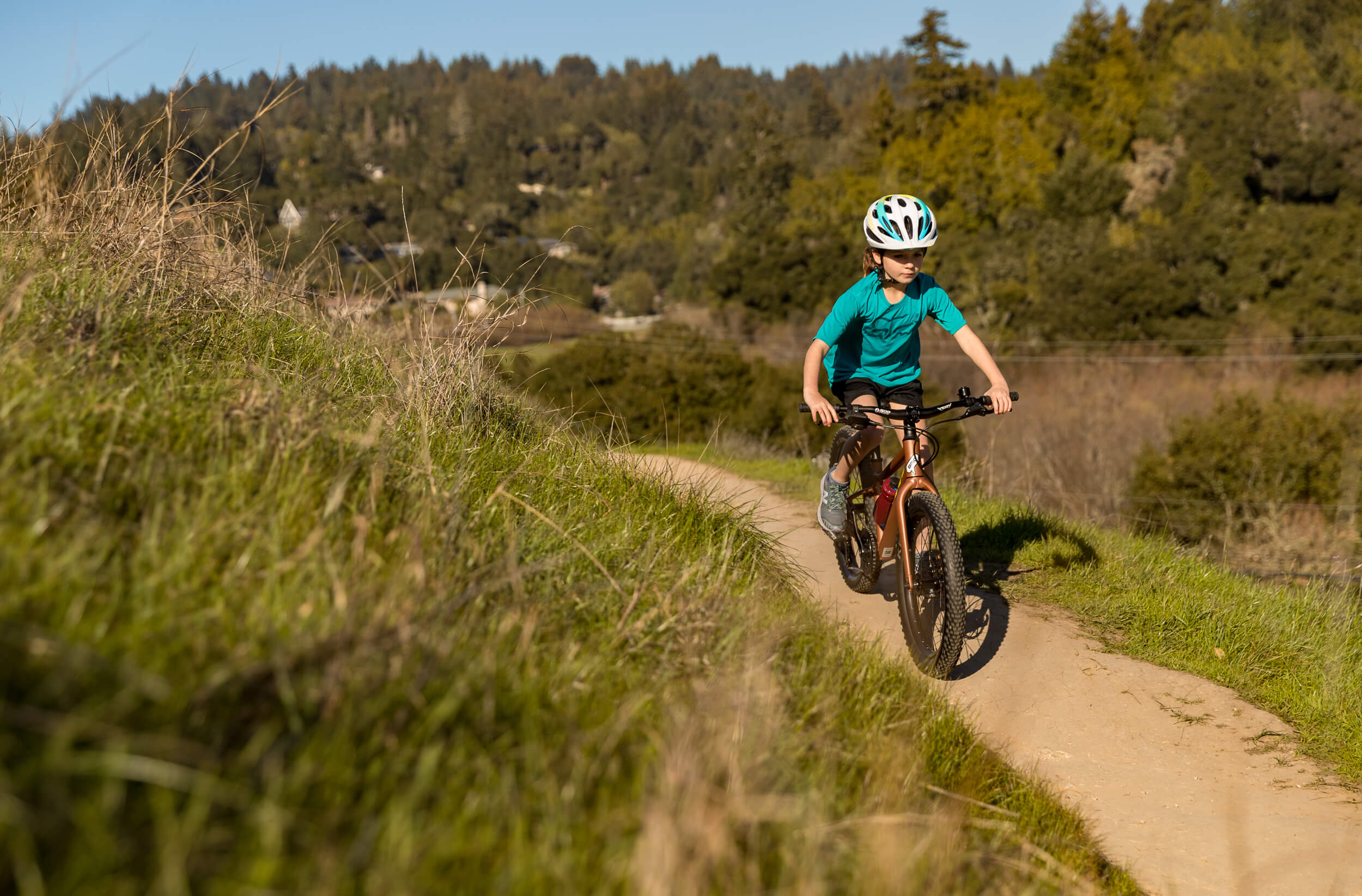 Kind auf Fahrrad mit Helm auf einem Waldpfad, für Kinder von 4-5 Jahren, bei sonnigem Wetter.