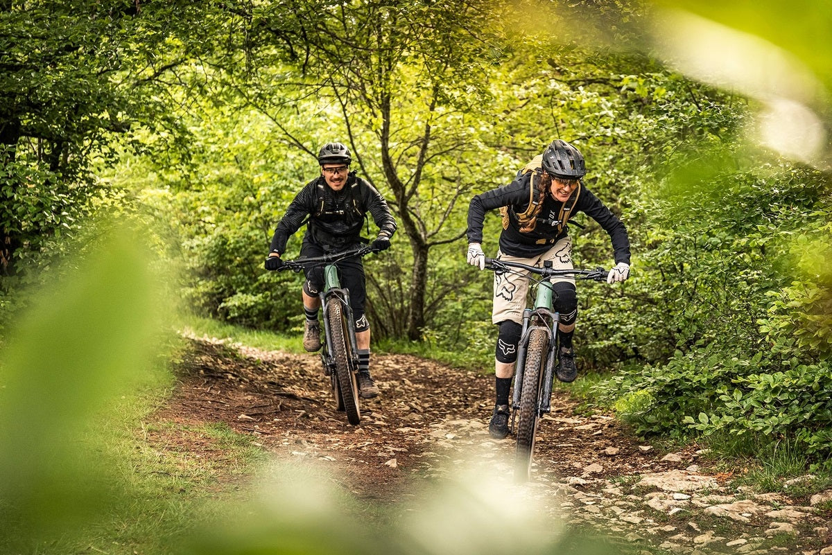 Zwei Personen fahren auf Focus E-Mountainbikes durch einen Waldpfad, ideal für Offroad-Enthusiasten.
