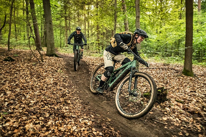 Mountainbiker fahren mit E-MTBs durch einen Waldpfad, Fokus auf Offroad-Abenteuer, geeignet für Outdoor-Enthusiasten.