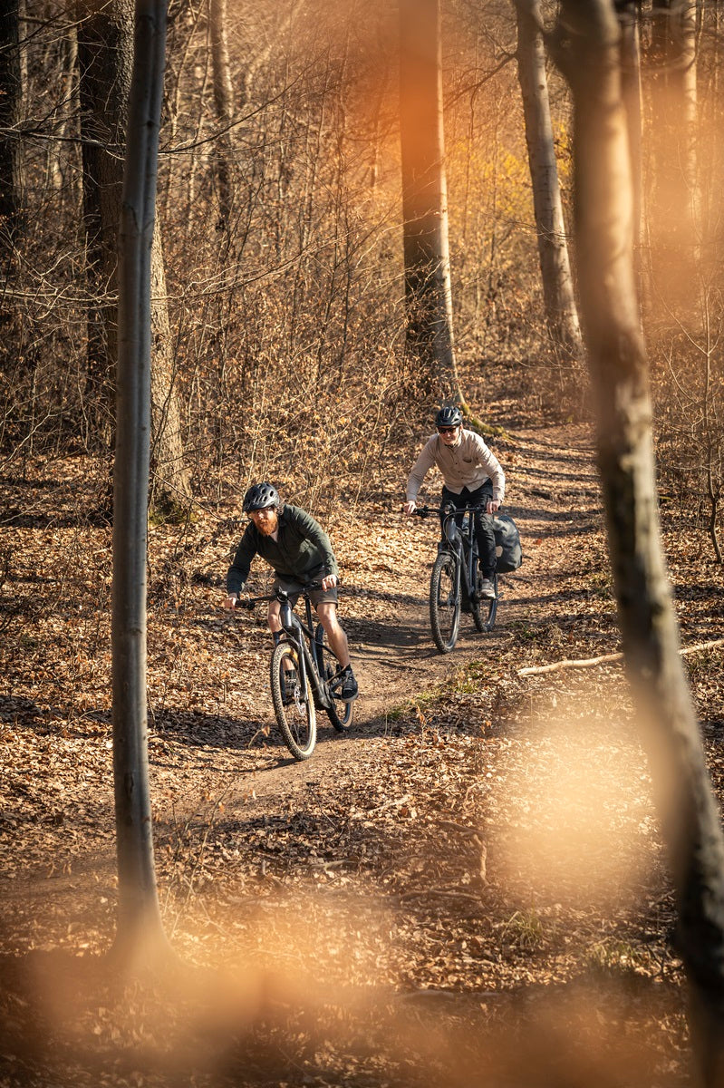 Zwei Radfahrer auf einem Waldpfad, fahren E-MTB-Hardtails durch herbstliche Landschaft, ideal für Offroad-Touren.