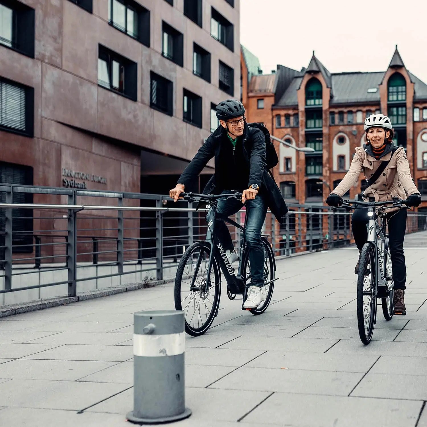 Zwei Personen fahren Specialized-E-Bikes in einer urbanen Umgebung, tragen Helme und Freizeitkleidung.