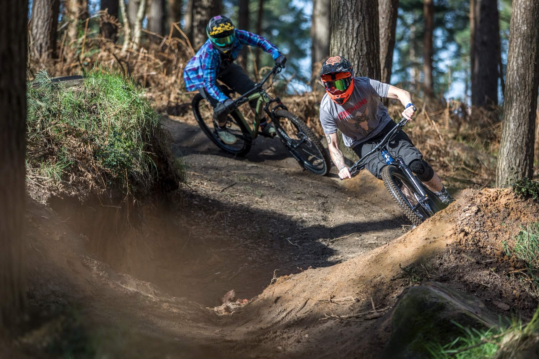 Zwei Mountainbiker auf einem Trail im Wald, mit Helm und Schutzkleidung; Thema: Abenteuer und Outdoor-Sport.