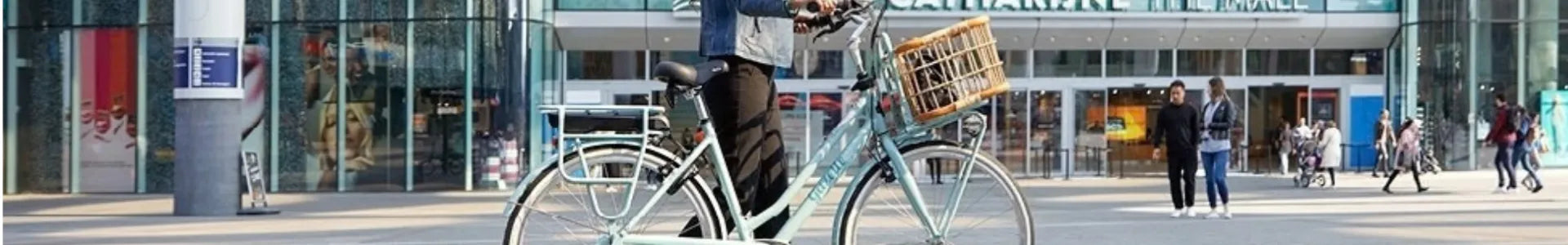 Person auf mintgrünem Gazelle Bike mit Korb vor Eingang eines Einkaufszentrums.