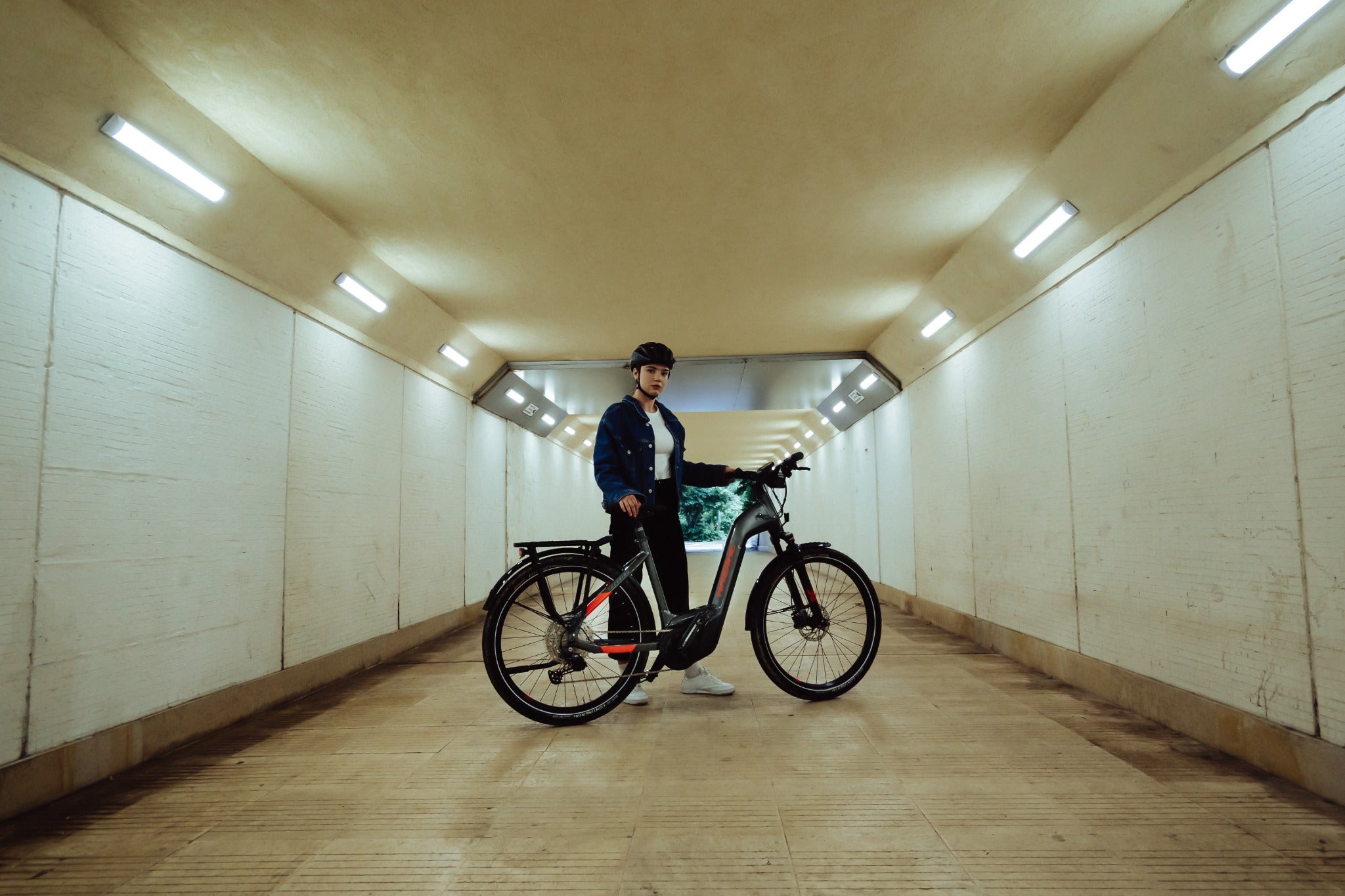 Person mit Helm steht in einem Tunnel neben einem Haibike E-Trekkingrad, ideal für städtische Touren und Pendler.