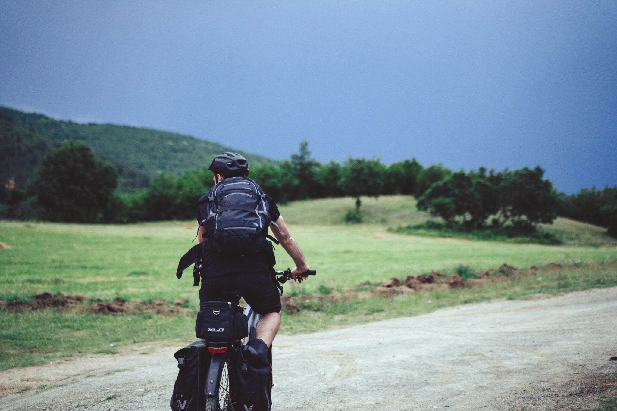 Mann mit schwarzem Helm und Rucksack auf Trekkingbike im Grünen, Marke Haibike, Modell nicht erkennbar. Ideal für Outdoor-Touren.