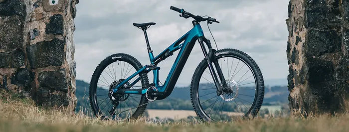 Blaues Cube Stereo Hybrid One44 zwischen zwei Steinsäulen, ideal für Offroad-Abenteuer. Markennamen und Modell nicht erkennbar.