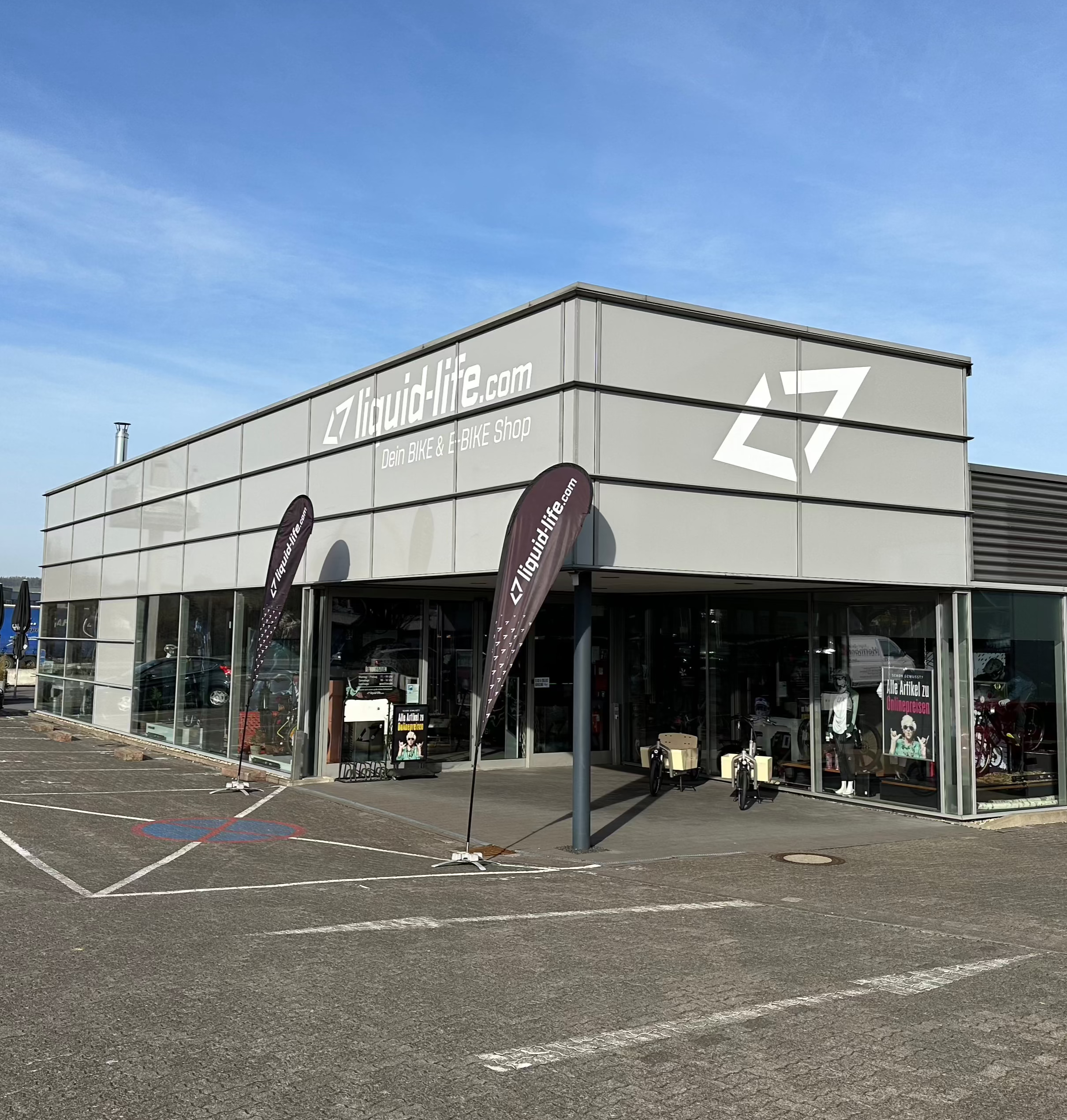 Fahrrad- und E-Bike-Shop Liquid-Life von außen, modernes Design, große Fenster und Werbeflaggen.