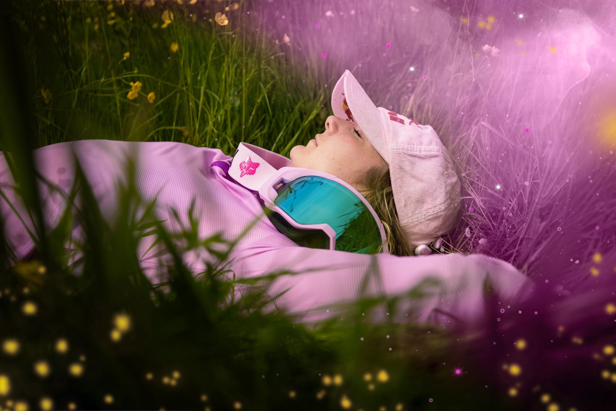 Person mit rosa Kappe und Fox-Brille im Gras liegend, entspannte Szene, Zielgruppe Outdoor- und Sportliebhaber.