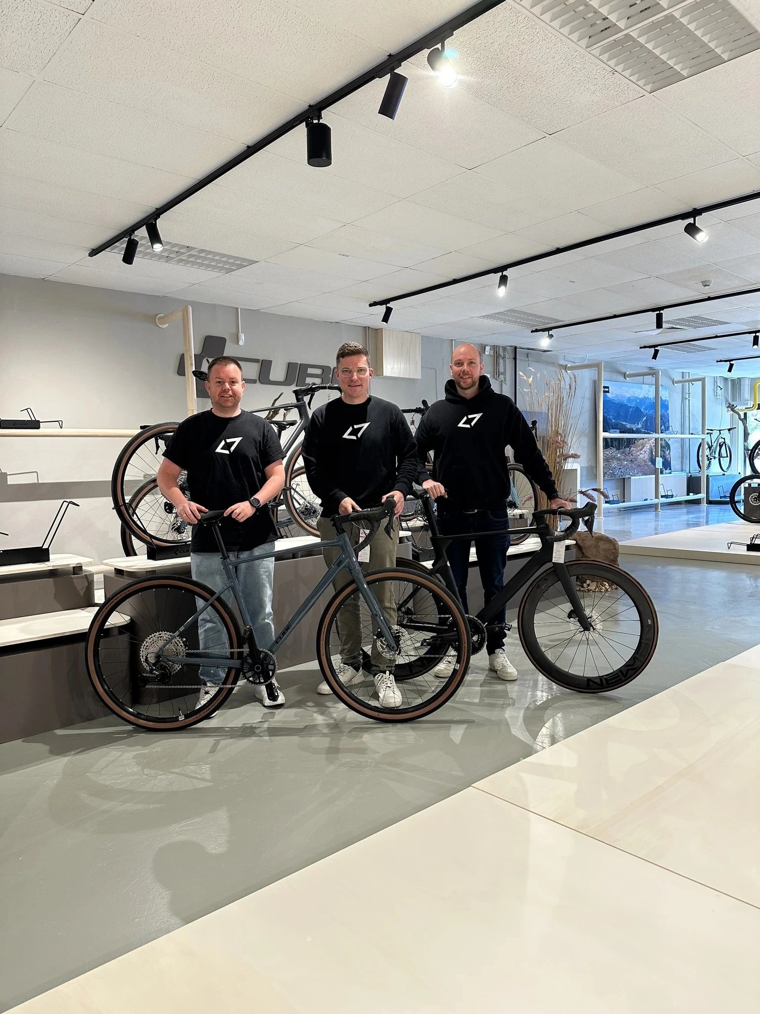 Drei Männer präsentieren Fahrräder im Ausstellungsraum von Cube-Store Lippstadt, moderne Räder für Sportbegeisterte.