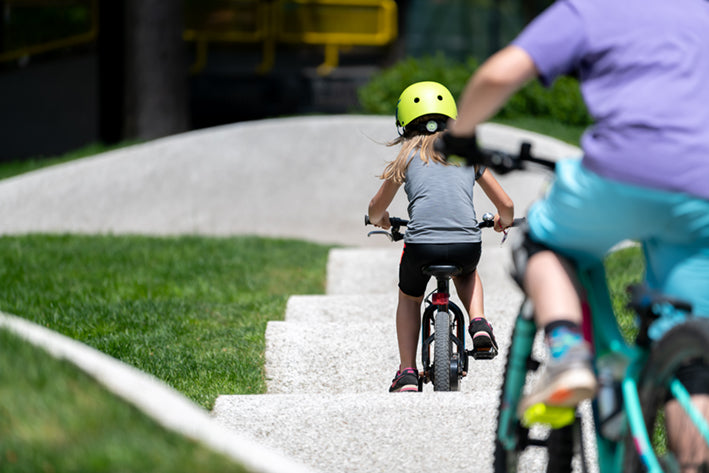 Kinder auf Spielplatz-Piste mit Fahrrädern, Helm. Zielgruppe: Kinder 3-4 Jahre. Fahrradfahren, Bewegung, Outdoor-Spaß.