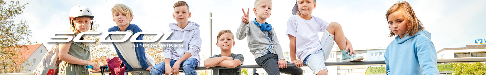 Kinder posieren auf einem Geländer mit Scool Junior Bikes Logo im Vordergrund. Kinderfreundliche Freizeitkleidung.
