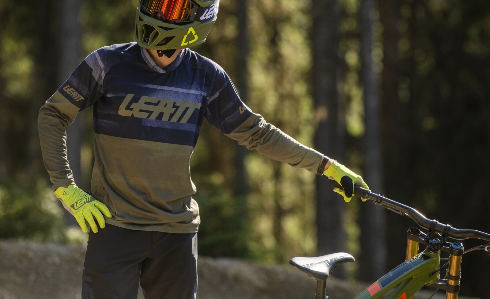 Motocross-Fahrer in Leatt-Bekleidung und Helm, hält Fahrradlenker im Waldgelände.
