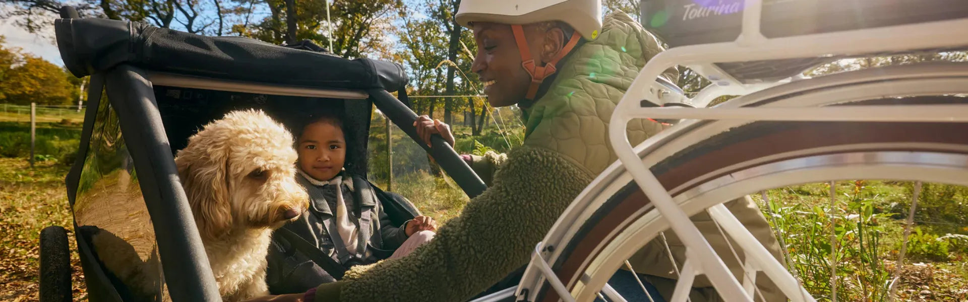 Kind und Hund in einem Croozer Fahrradanhänger für Kinder neben einem Erwachsenen mit Helm. Ideal für Familienausflüge.