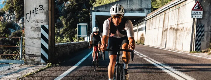 Zwei Männer fahren ein Superior Rennrad auf einer Landstraße unter einer Brücke, beide tragen Sportbekleidung und Helme.