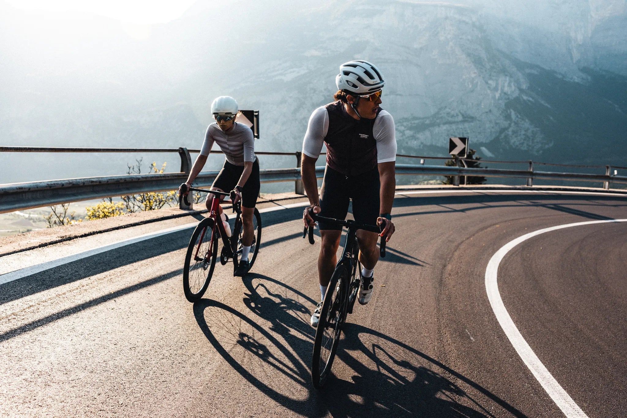 Zwei Superior Rennradfahrer in Schutzkleidung fahren auf einer kurvigen Bergstraße, umgeben von malerischer Berglandschaft.