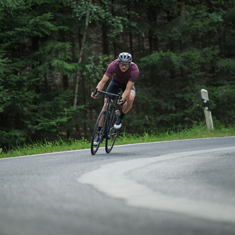 Mann auf Cube Attain Rennrad fährt auf kurviger Landstraße durch Wald, ideal für sportliche Radfahrer.