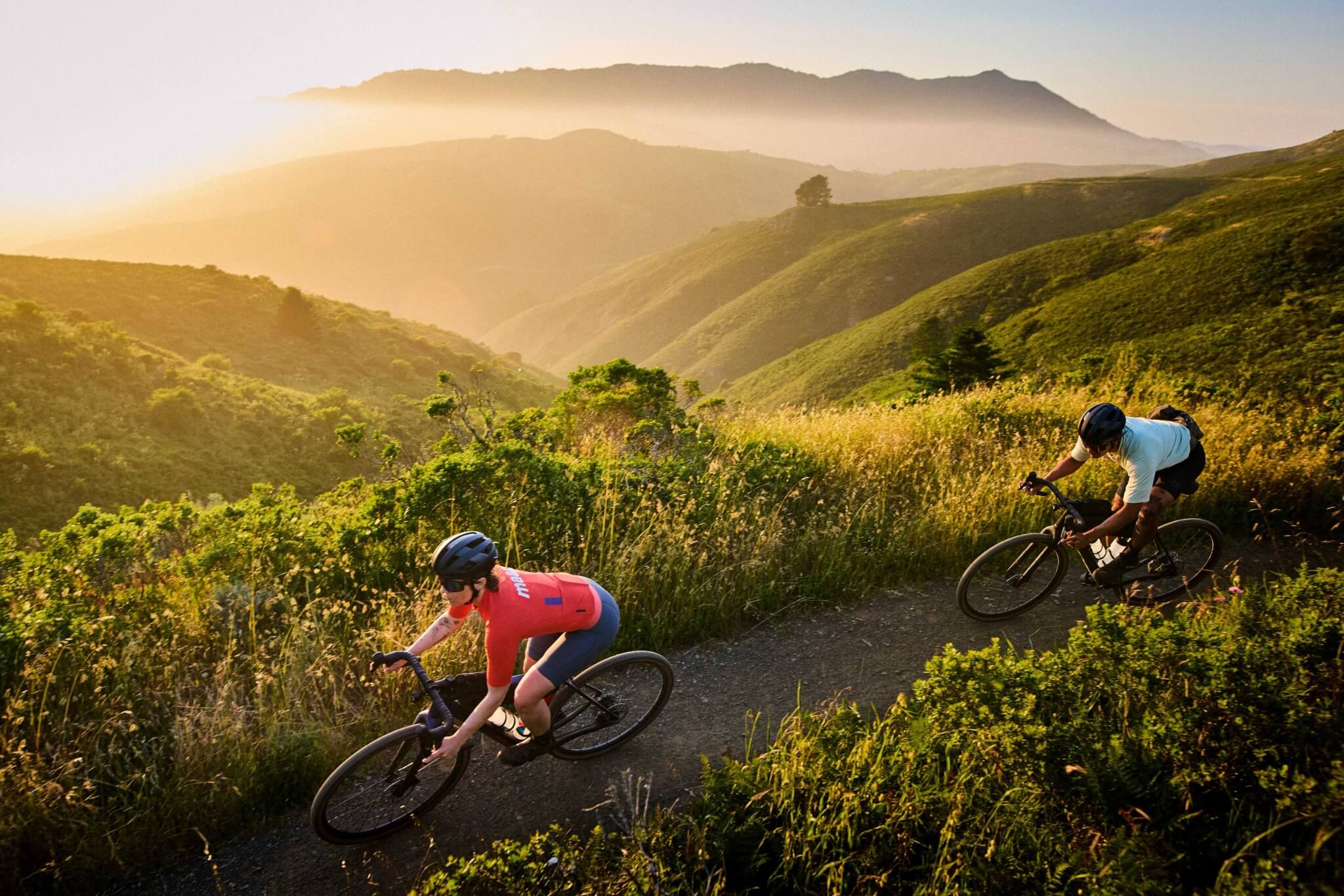 Zwei Personen fahren Trek Checkpoint Fahrräder auf einem Pfad in hügeliger Landschaft bei Sonnenaufgang.