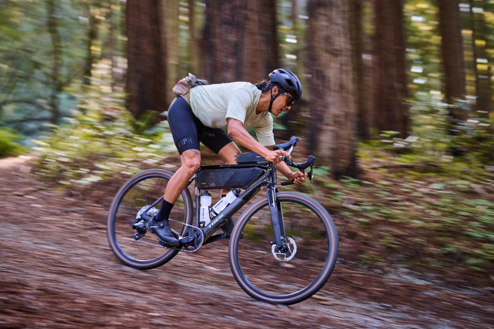 Fahrradfahrer in sportlicher Kleidung fährt ein Trek-Checkpoint Gravelbike durch bewaldetes Gelände.